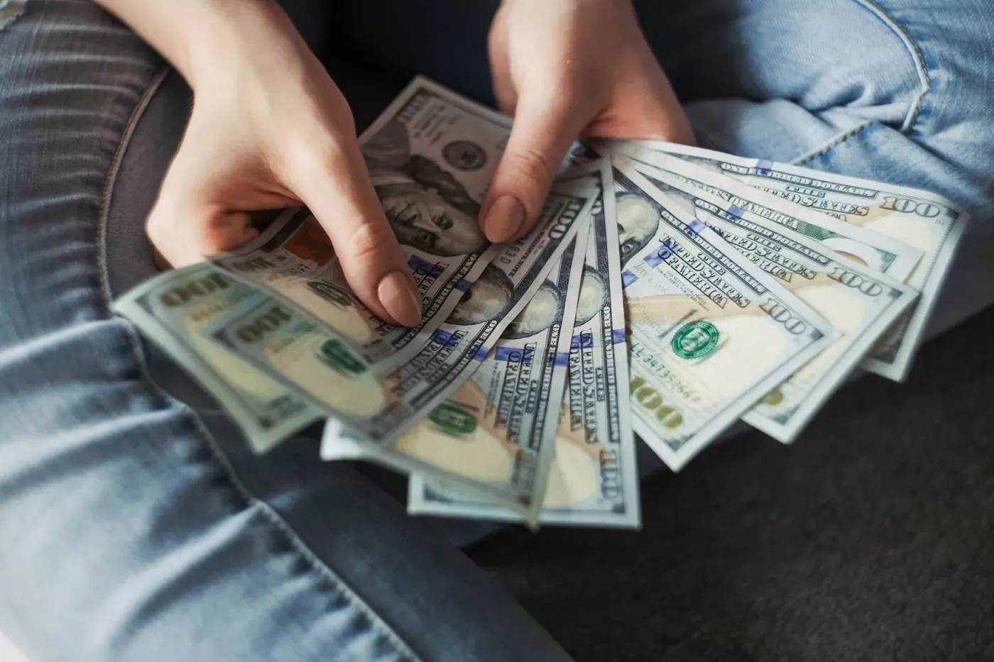 أيدٍ تمسك مروحة من أوراق نقدية أمريكية من فئة المئة دولار